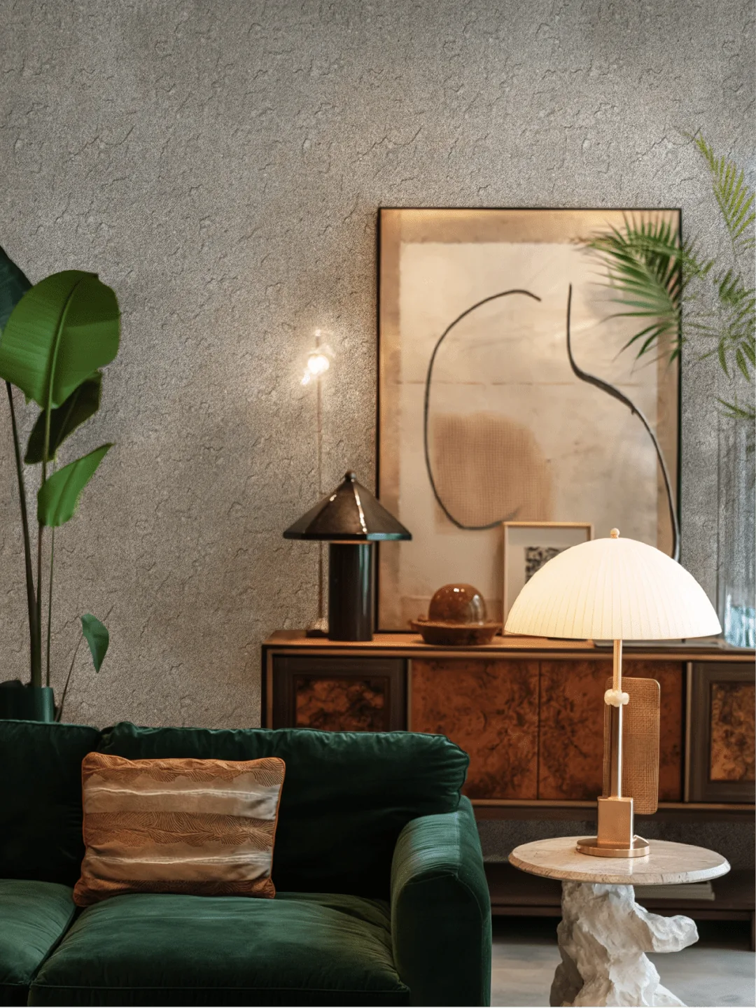 A plush green sofa sits beside a marble side table with a pleated lamp in a modern living room.