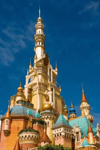 A fairytale castle with colorful spires and domes stands tall against a bright blue sky.