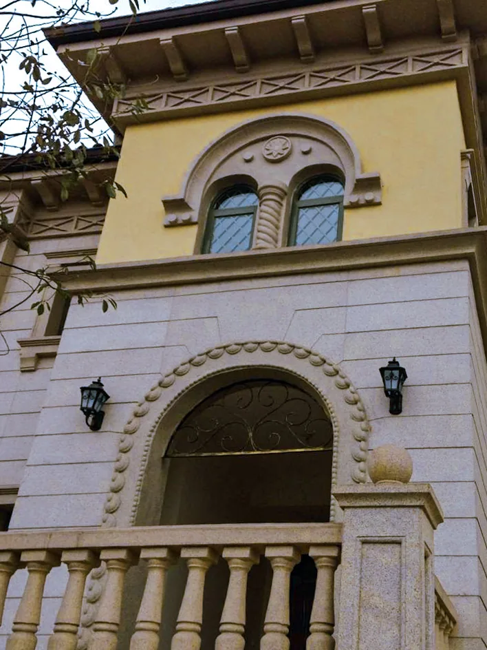 Ornate arched entryway with decorative ironwork and a stone balustrade on a yellow building.